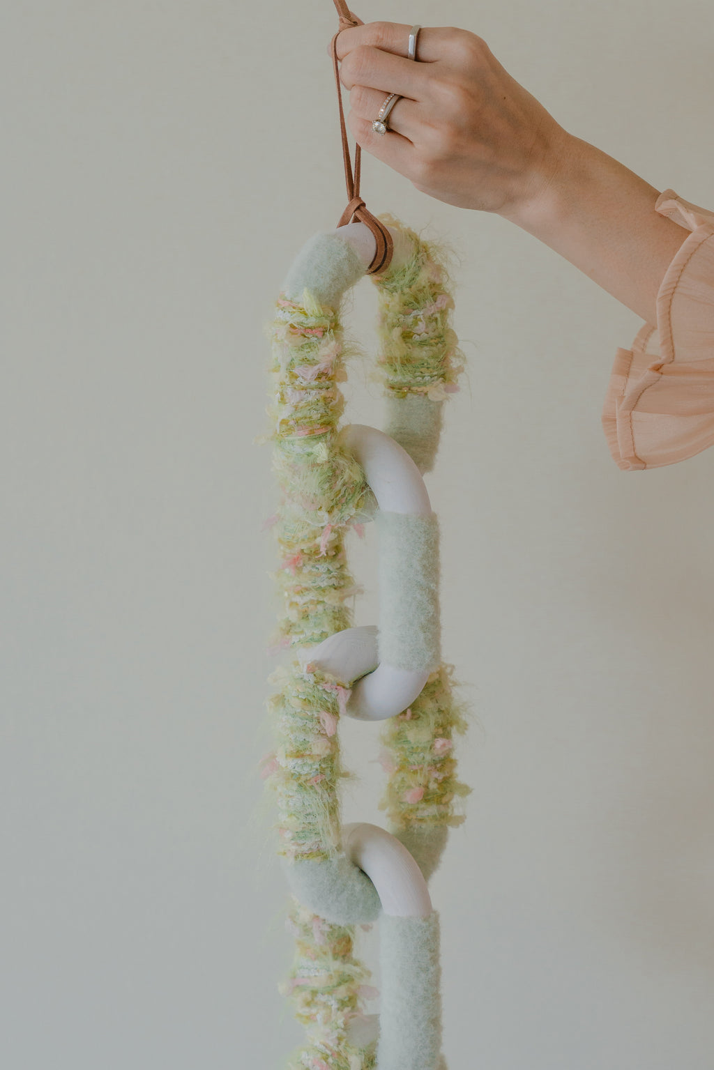 Close-up of Passing By Blooms Valley: textured threads of muted green and ivory yarn interlaced with leather to evoke a blooming valley.