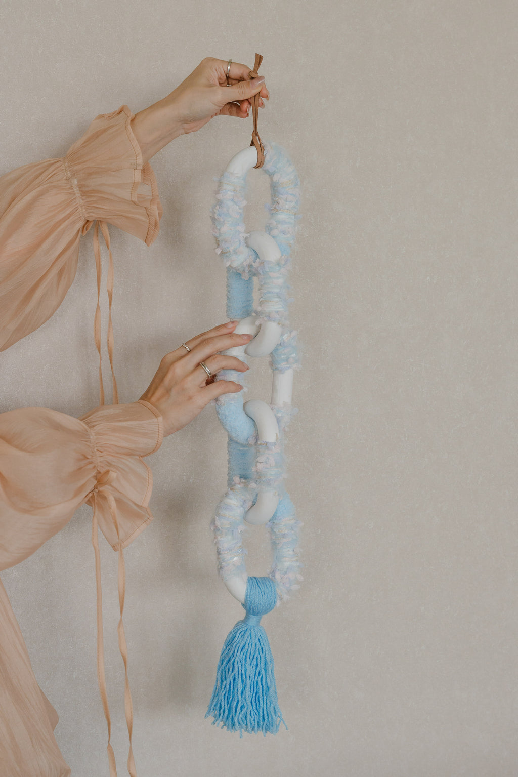 Passing By Blooms Delphinium fibre wall art — delicate yarn in lavender and periwinkle tones woven with leather accents, evoking drifting spring blossoms.