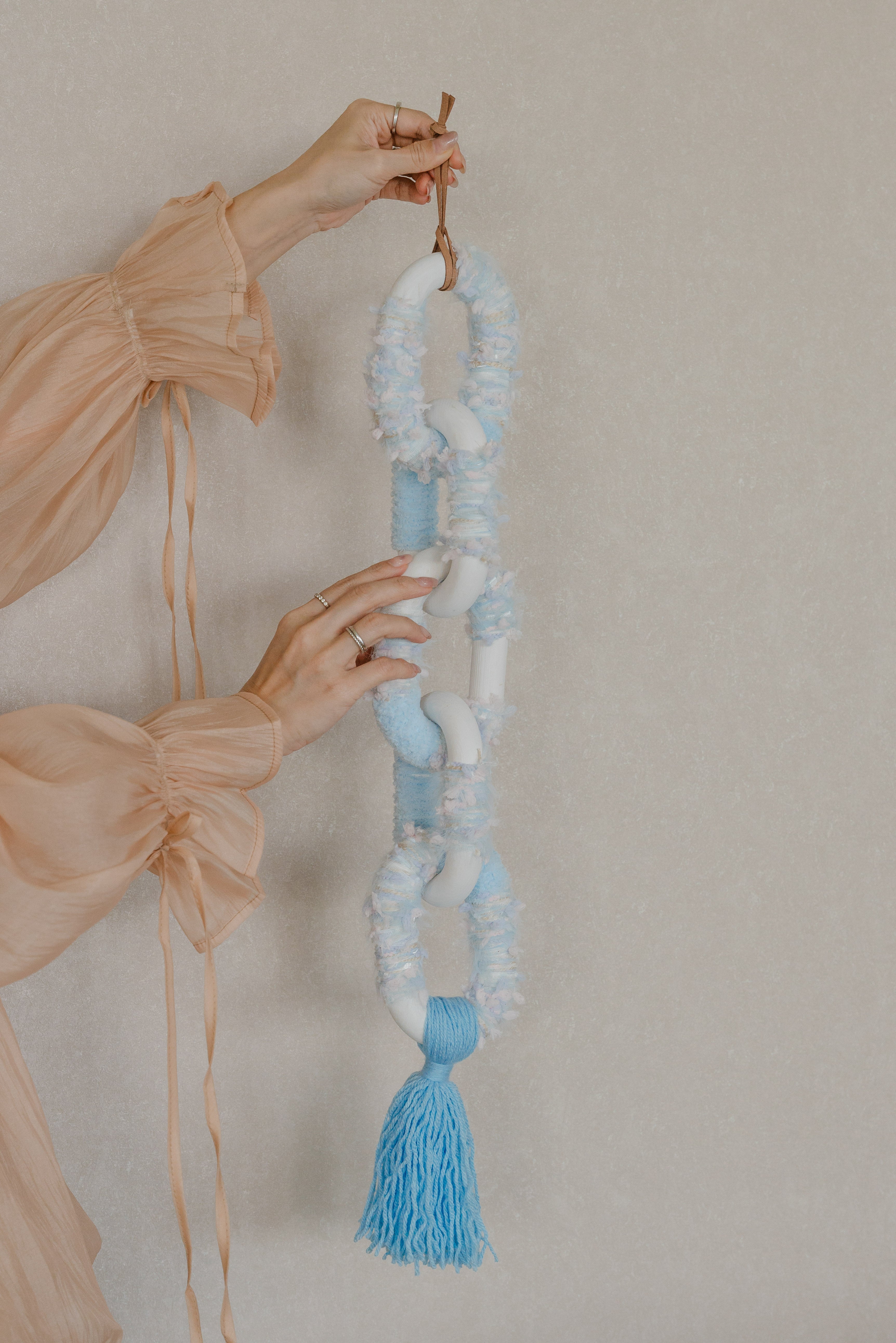 Passing By Blooms Delphinium fibre wall art — delicate yarn in lavender and periwinkle tones woven with leather accents, evoking drifting spring blossoms.