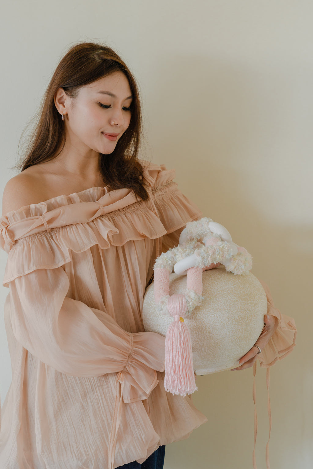 Passing By Blooms Rose displayed on a neutral wall, its pale pink yarn and leather detail adding subtle warmth and organic texture.