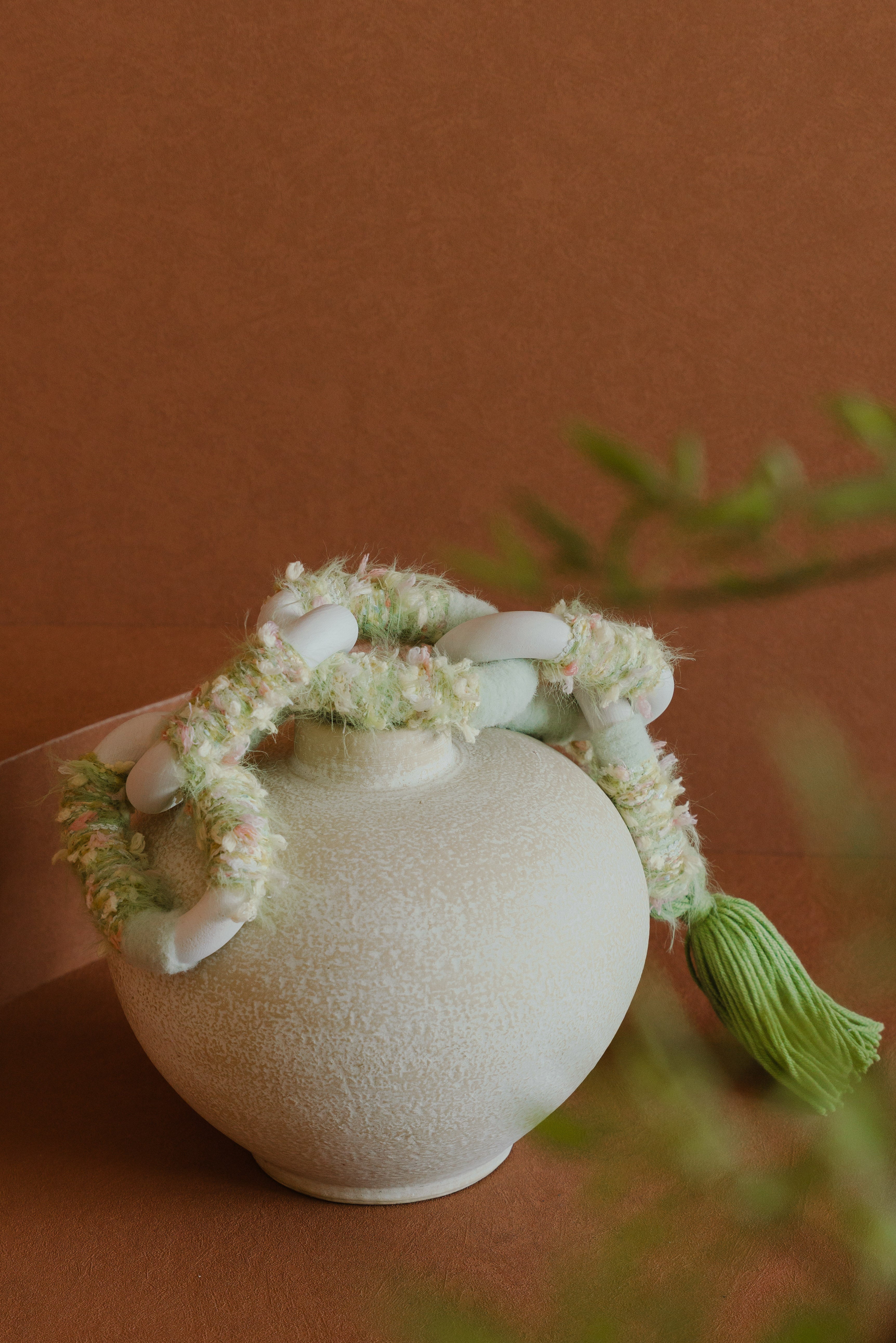 Passing By Blooms Valley fibre wall art — layered yarn in soft sage and cream tones, woven with leather accents for gentle floral texture.