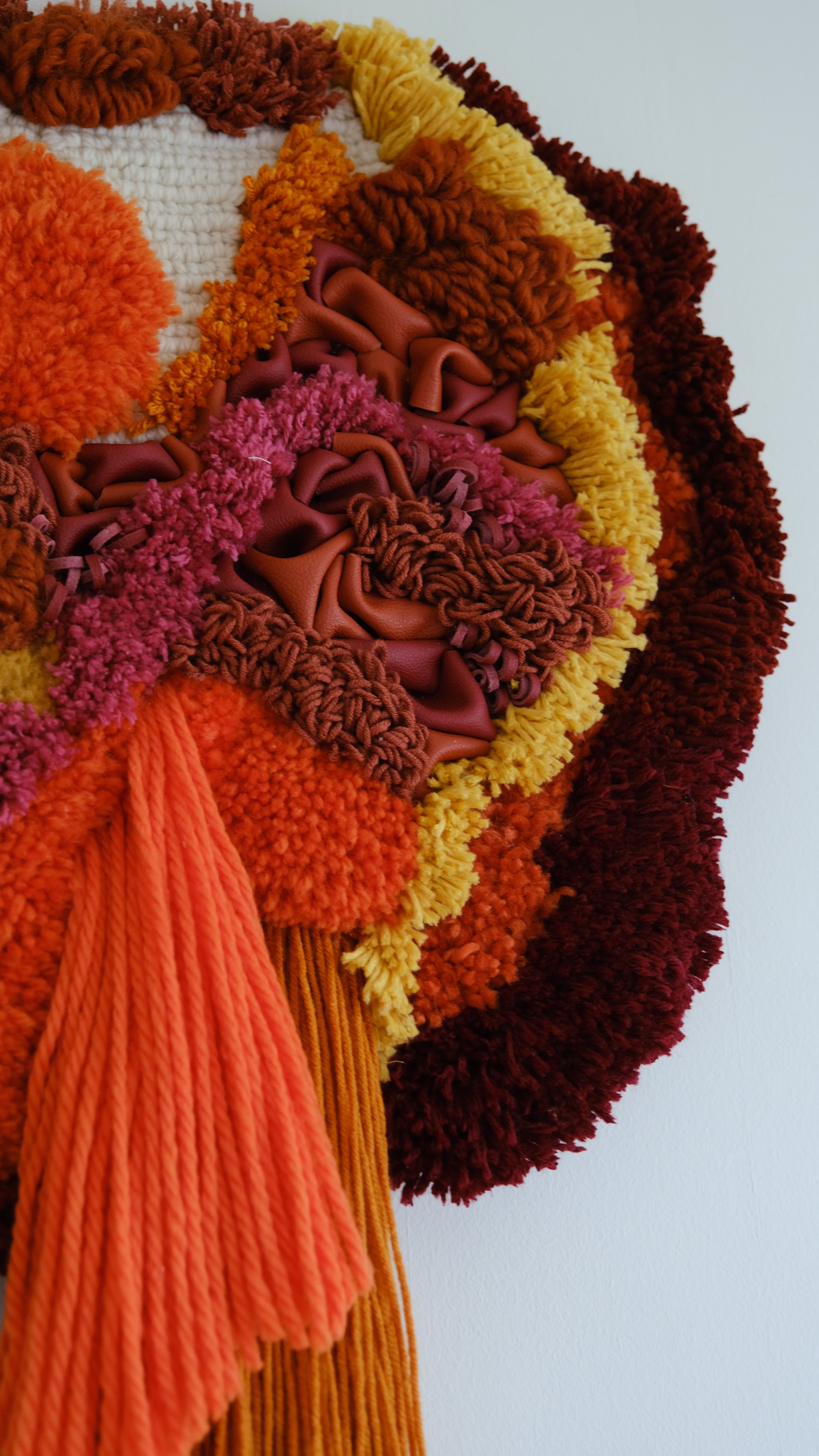 Close-up of Ascend fibre art: warm mustard and orange yarn woven with leather accents, capturing sunrise over rugged mountains.